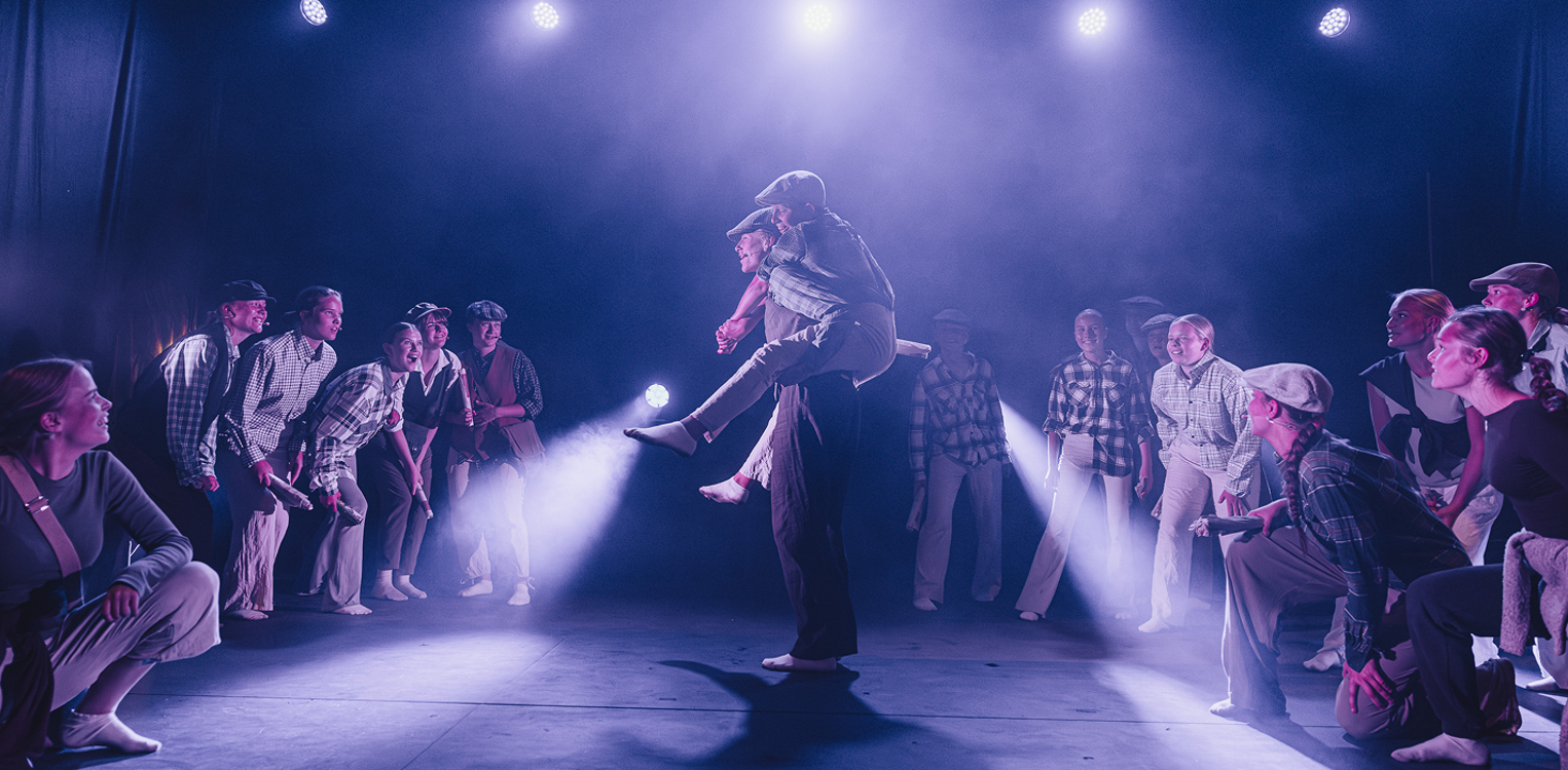 Ungdommer på en scene, der en gutt bærer en annen på ryggen mens flere står rundt dem.