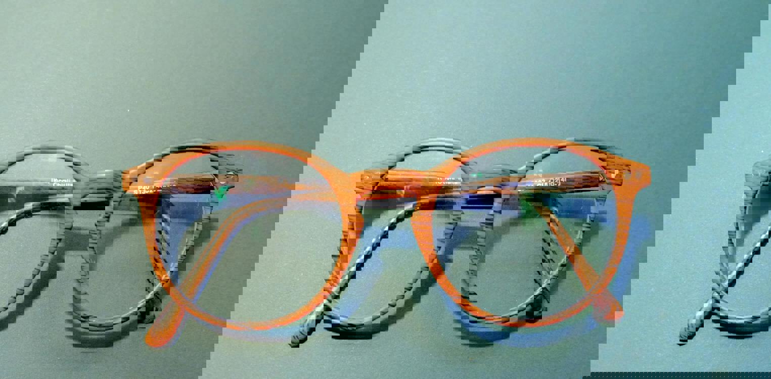 Brune briller med trelook ligger mot en grønn bakgrunn. Bilde av Alizee Marchand: https://www.pexels.com/nb-no/bilde/947885/