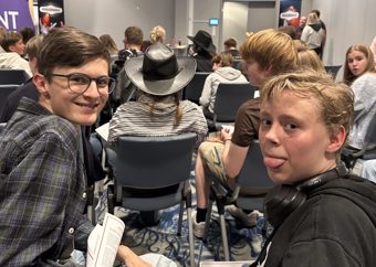 Ungdommer sitter på stoler og ser fremover; to gutter bakerst ser mot kamera, én smiler og den andre gjeiper.