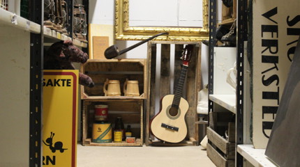 Rekvisitter på et teaterlager, med skilt, instrumenter og ulike rekvisita stablet i hyller.
