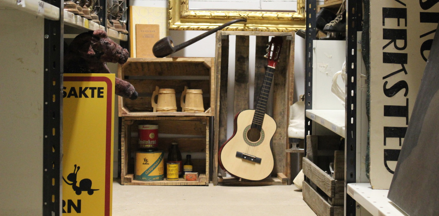 Rekvisitter på et teaterlager, med skilt, instrumenter og ulike rekvisita stablet i hyller.