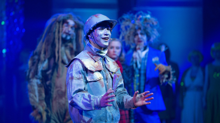 Blikkmannen fra Trollmannen fra Oz synger, med de andre karakterene stående i bakgrunnen.